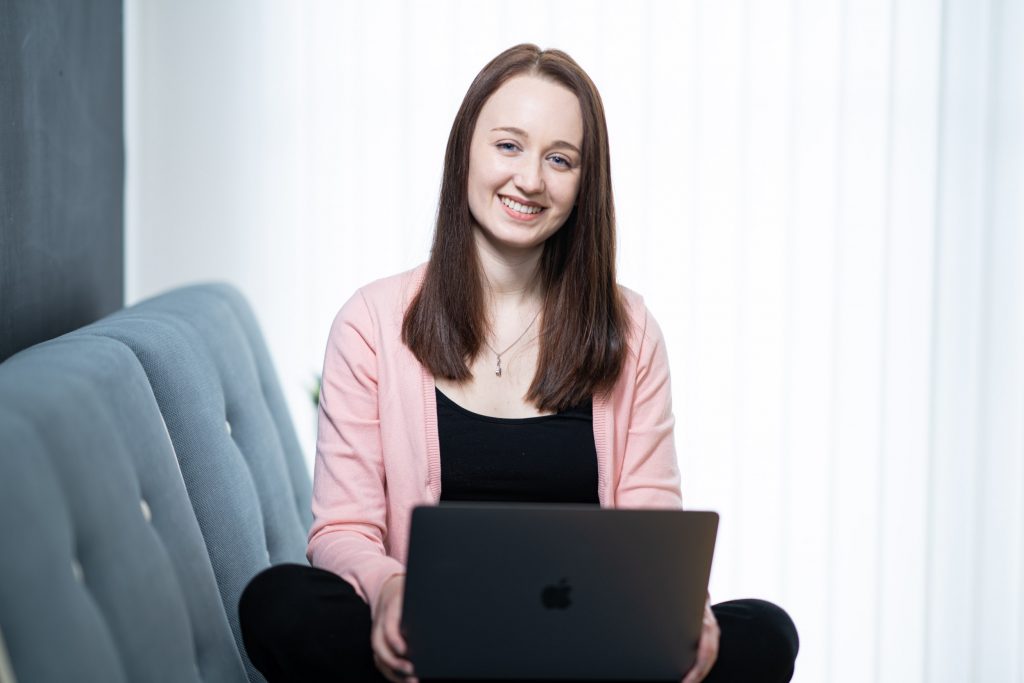 Pippa Stacey Disability blogger sits on a sofa using a laptop smiling to camera