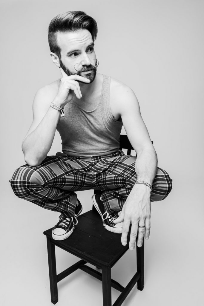 Portrait photography of Christian Carlisle, he is squatting on a chair in black and white 